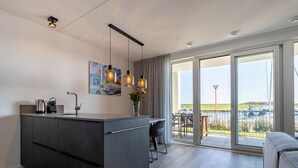 Eine moderne Küche mit einer zentralen Kochinsel, ein Essbereich mit Blick ins Freie und ein Balkon mit Geländer.