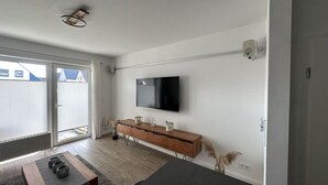 A modern bedroom with a large bed, a TV mounted on the wall, a wooden dresser, and a sliding glass door leading to a balcony. - Huus Rehders Modern Retreat (Büsum)