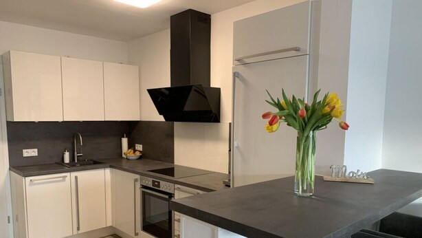 A modern kitchen with white cabinets, a black range hood, and a built-in oven. - Huus Rehders Modern Retreat (Büsum)