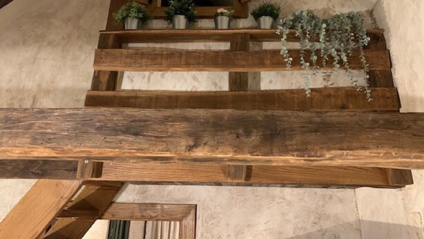 Un escalier en bois, avec un miroir au-dessus et de petites plantes en pot sur les marches.