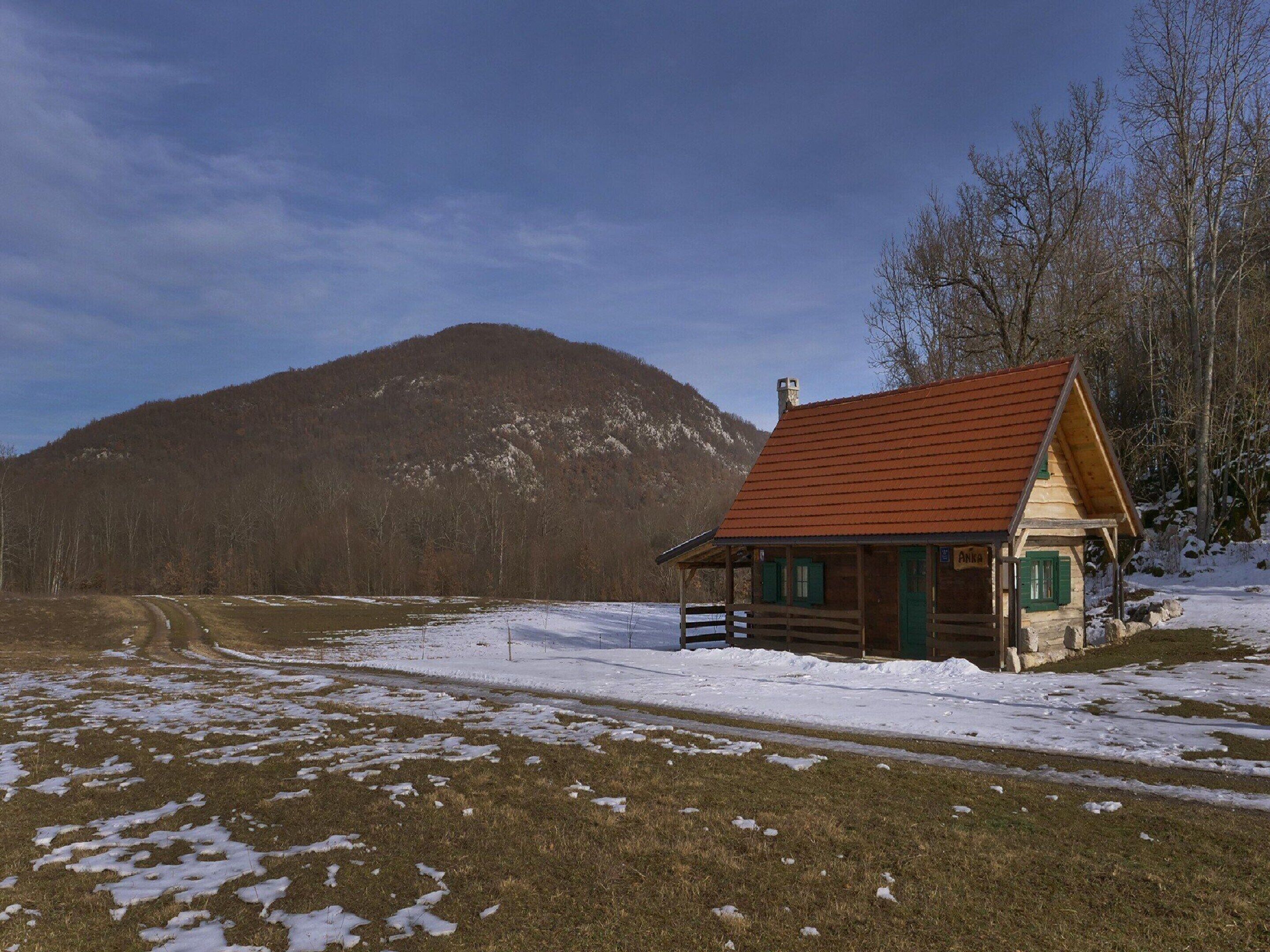 A wooden cabin with a red roof, surrounded by a snowy landscape and a mountain in the background.