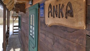 Une enseigne en bois portant le nom « ANKA » gravé dessus, fixée à un bâtiment rustique avec une porte verte et un chemin de pierre menant à l’entrée.