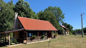 Une cabane rustique avec un toit rouge, une cheminée en pierre et une véranda dotée de chaises vertes.