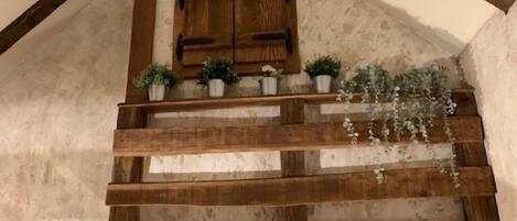 A wooden staircase with a rustic design, leading to a landing with a wooden door and potted plants.