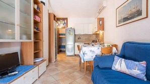 Ett kompakt bostadsutrymme med ett litet kök, en matplats och en soffa med en prydnadskudde i marint tema.