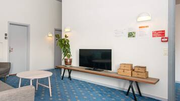 Un área de recepción con un televisor de pantalla plana, un banco con cestas, una planta en maceta y una pequeña mesa redonda.