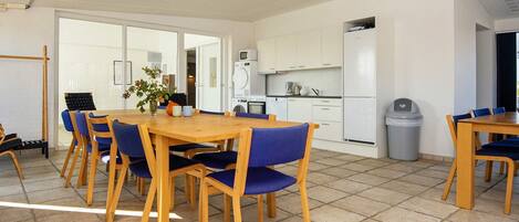A modern kitchen with white cabinets, a microwave, and a refrigerator. There is a dining area with a wooden table and blue chairs.