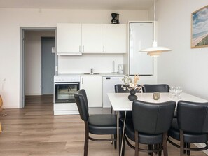 A modern kitchen with white cabinets, a built-in oven, and a dining area with a white table and black chairs. - 4 Person Holiday Park Home in Ulfborg (Ulfborg)