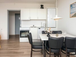 A modern kitchen with white cabinets, a built-in oven, and a dining area with a white table and black chairs.