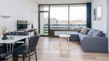 A modern living room with a dining area, a sofa, a TV, and a view of a distant landscape through large windows.
