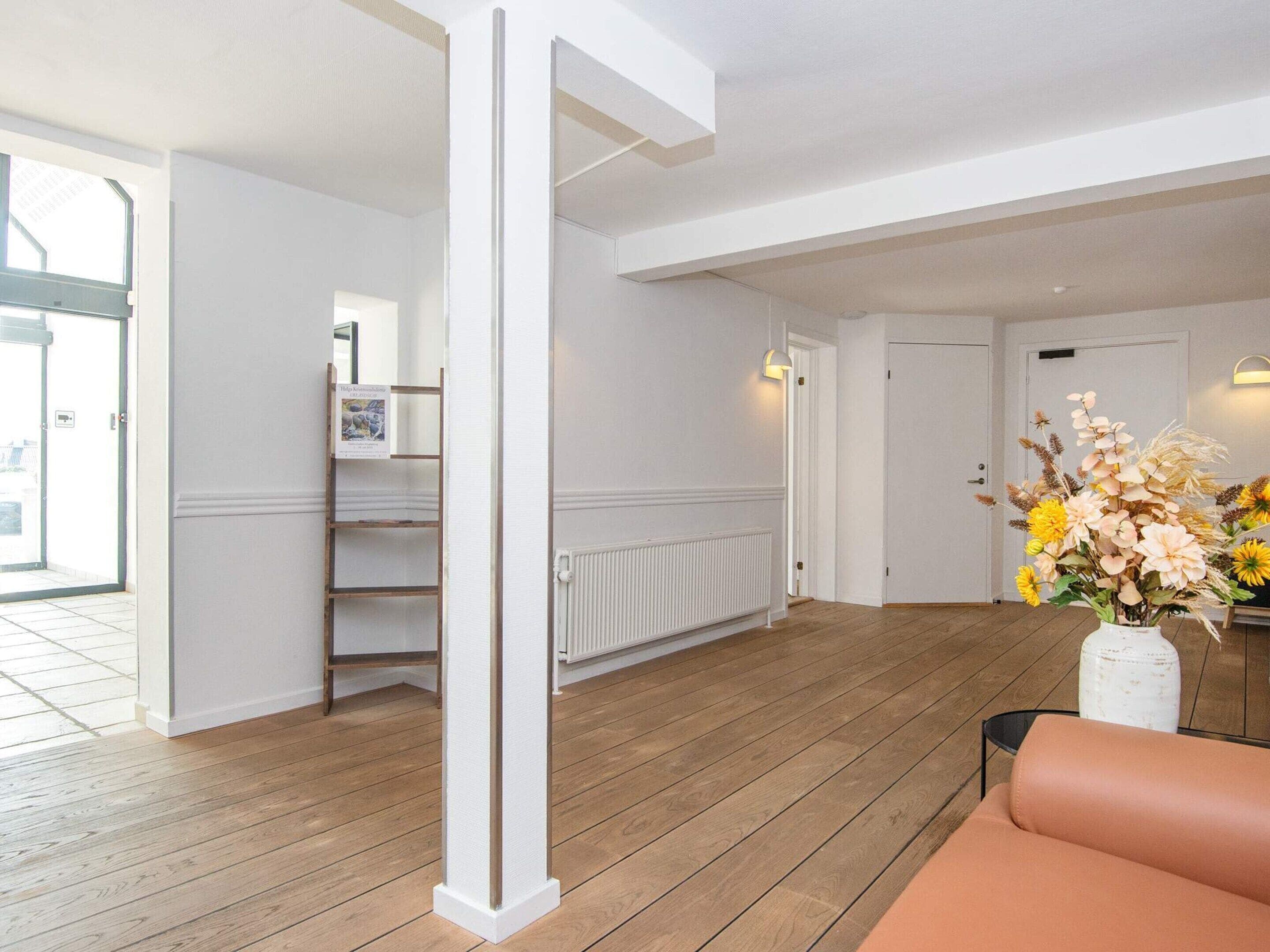 A spacious room with wooden flooring, a white radiator, a white door, and a small shelf with a picture frame.