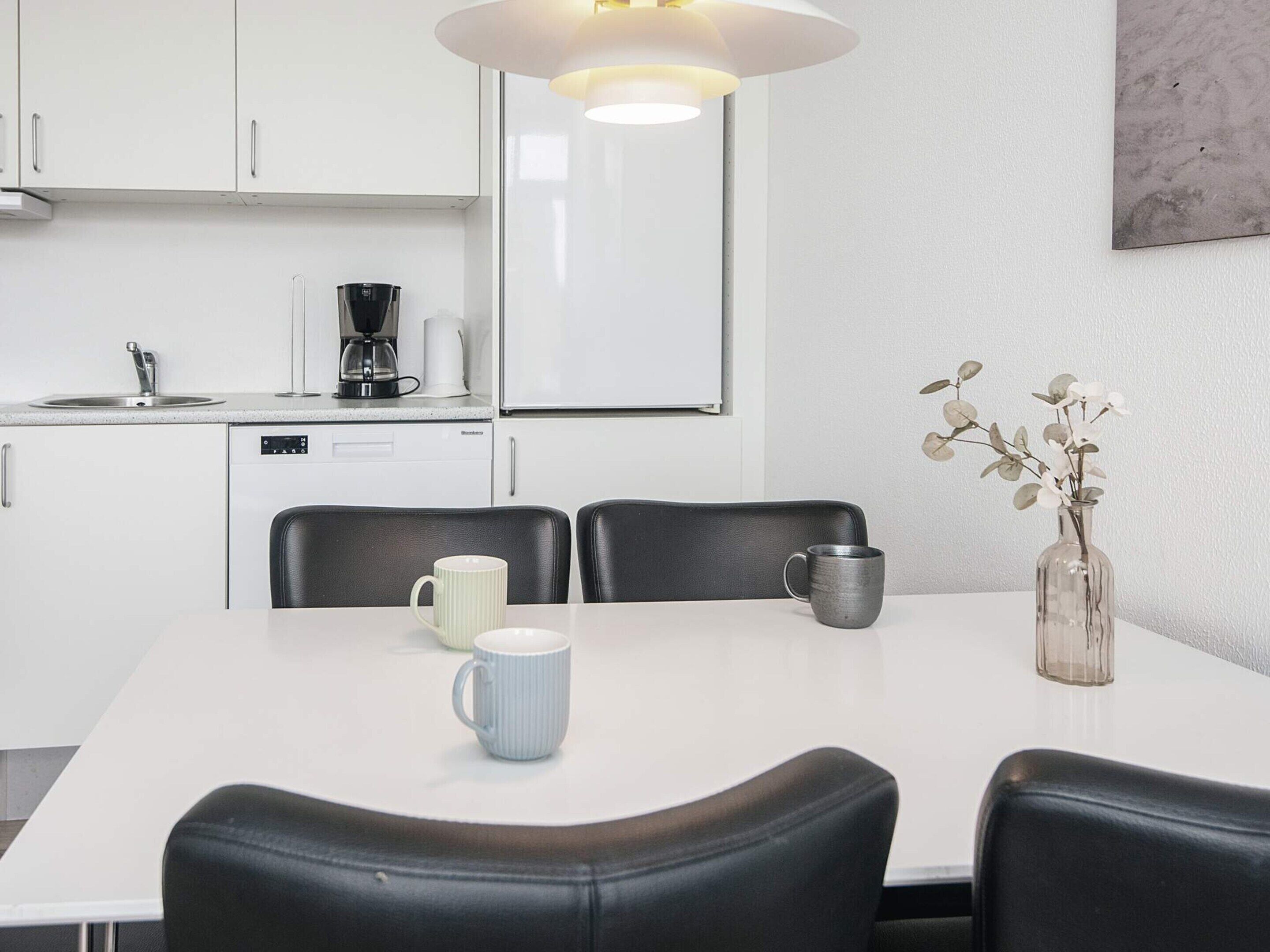 Una cocina moderna con armarios blancos, una cafetera y una mesa de comedor con sillas.
