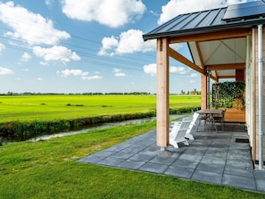 A covered outdoor seating area with a view of a green field and a small water channel. - Holiday Home With an Unobstructed View (Akkrum)