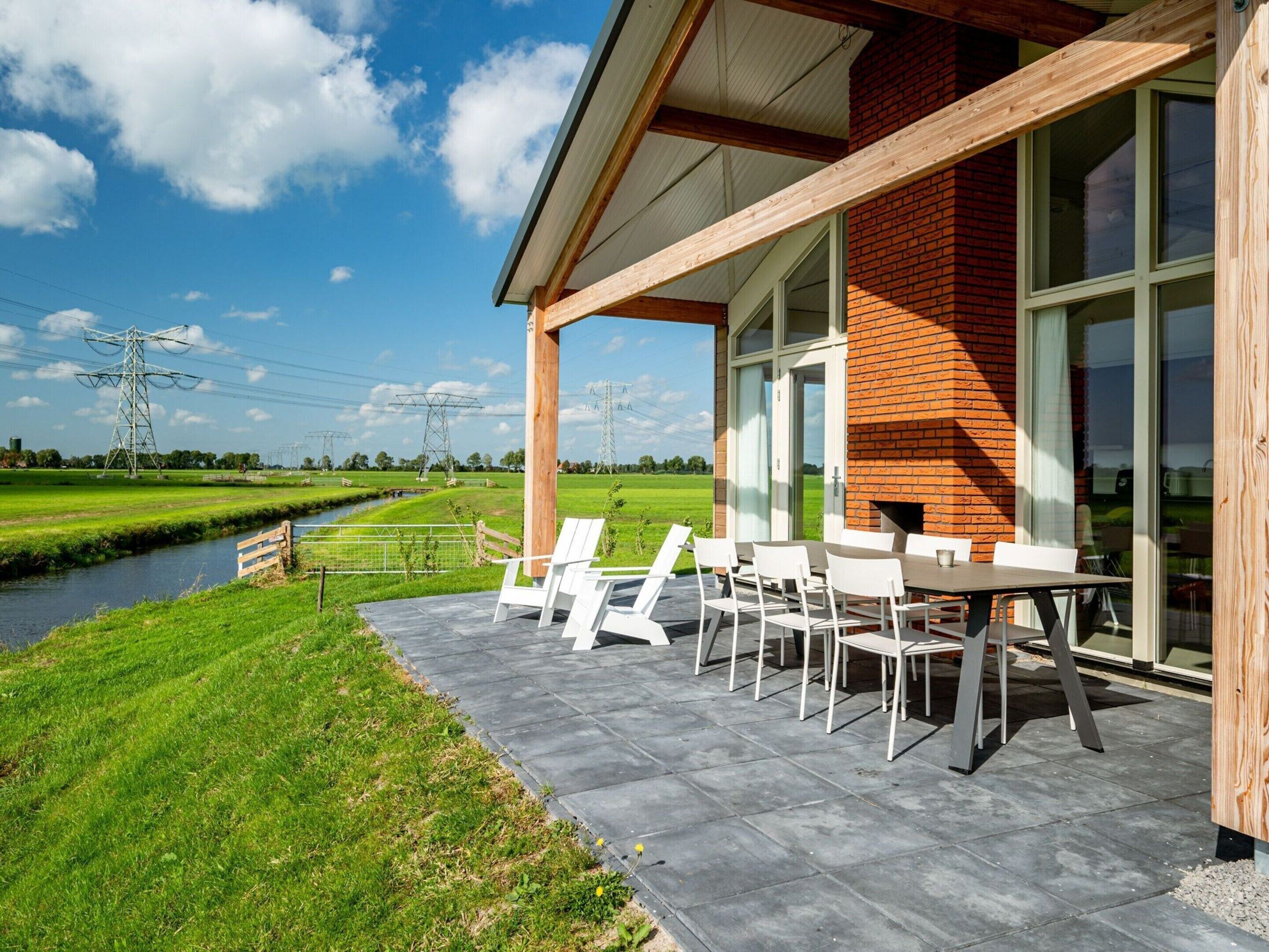 Eine moderne Außenpatio mit Backsteinmauer, großen Fenstern und Blick auf ein grünes Feld sowie Stromleitungen.