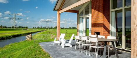 Eine moderne Außenpatio mit Backsteinmauer, großen Fenstern und Blick auf ein grünes Feld sowie Stromleitungen.