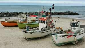 Varias embarcaciones amarradas en una playa arenosa, con un rompeolas rocoso al fondo.