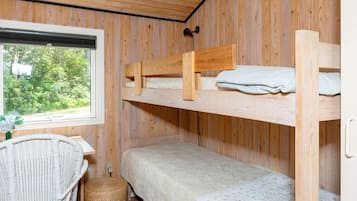 A bunk bed room with a window, a wicker chair, and a small table.