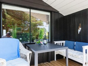 An outdoor seating area with a table and chairs, a large window, and a black wall. - 4 Person Holiday Home in Hjorring (Hjørring)