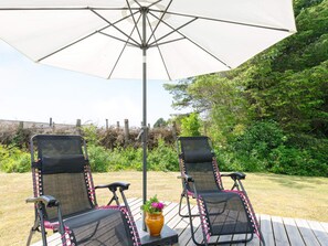 Two outdoor lounge chairs under a large umbrella, with a wooden deck and a garden in the background. - 4 Person Holiday Home in Hjorring (Hjørring)