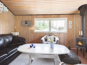 A cozy room with a wooden interior, a white table, a black leather sofa, a small armchair, a wall-mounted radio, and a wood-burning stove. - 4 Person Holiday Home in Hjorring (Hjørring)