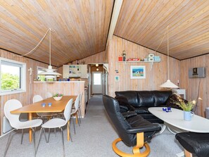 A modern cabin interior with a wooden ceiling, a dining area with a wooden table and white chairs, a black leather sofa, and a small white table with a vase. - 4 Person Holiday Home in Hjorring (Hjørring)