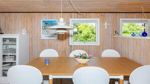A dining area with a wooden table, white chairs, a hanging light fixture, and a window with a view of greenery. - 4 Person Holiday Home in Hjorring (Hjørring)