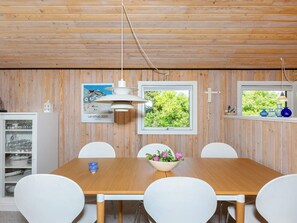 A dining area with a wooden table, white chairs, a hanging light fixture, and a window with a view of greenery. - 4 Person Holiday Home in Hjorring (Hjørring)