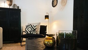 Uma sala de estar moderna com um sofá preto, uma almofada decorativa estampada, uma mesa pequena com uma tigela ornamental e um recipiente de vidro com plantas.