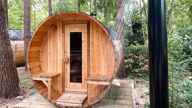 Uma estrutura de sauna de madeira com porta e bancos, cercada por árvores.