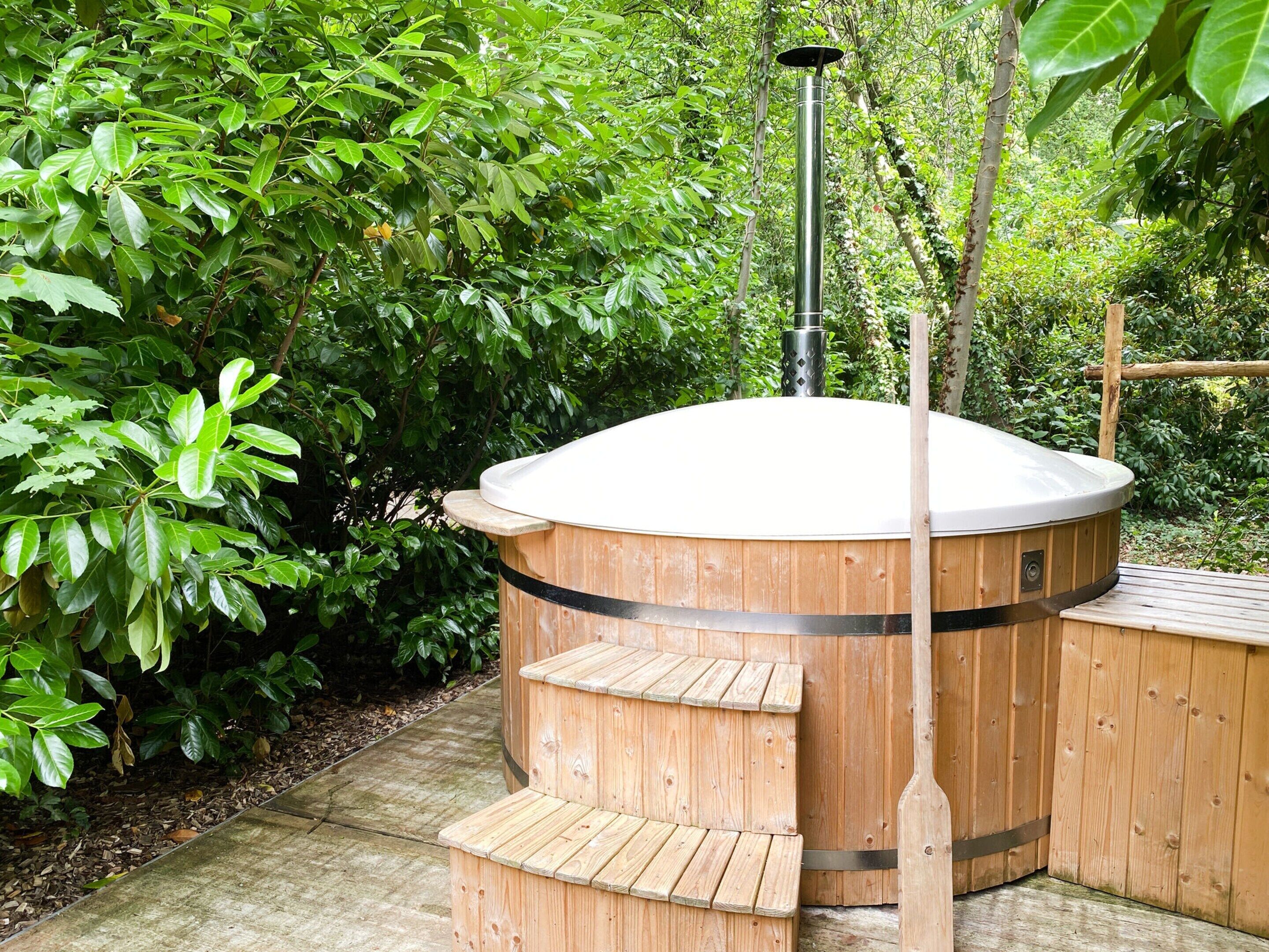 Un bain à remous avec une structure extérieure en bois et un couvercle blanc, entouré d’une végétation luxuriante.