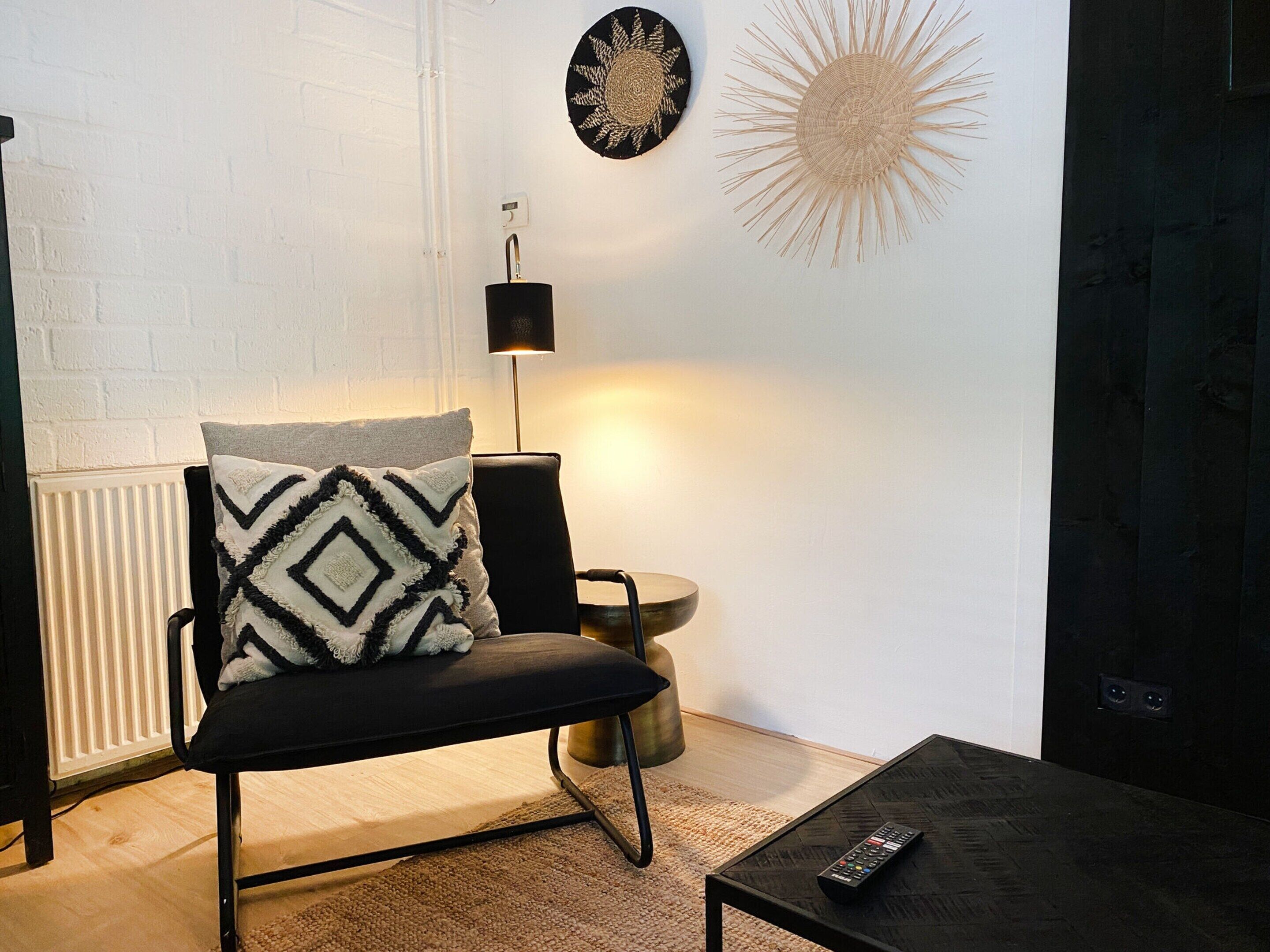 Un salón moderno con una butaca negra, una mesa redonda y una lámpara de pared.