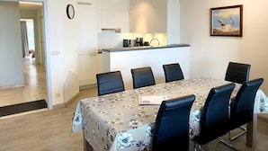 A modern dining area with a table set for six, a kitchen in the background, and a painting on the wall. - Apartment in Nieuwpoort Near the Beach (Nieuwpoort)