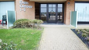 The entrance to Den Oever 1-2, featuring a brick facade, a glass door, and a paved pathway leading to the entrance. - Apartment in Nieuwpoort Near the Beach (Nieuwpoort)