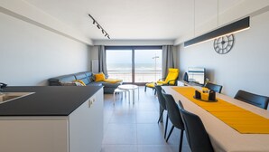 A modern hotel room with a kitchen, dining area, and a balcony with a view of the sea.