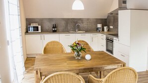 A modern kitchen with white cabinets, a wooden dining table, wicker chairs, and a hanging pendant light. - Apartment in Oberkirch (Oberkirch)