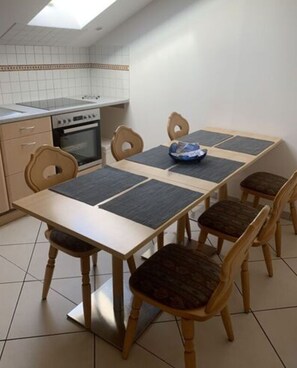 A dining area with a table and chairs, a kitchen with a stove and oven, and a skylight above. - Holiday Apartment Leiner (Garmisch-Partenkirchen)