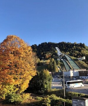 A view of a building with a curved roof, surrounded by trees with autumn foliage, and a bus in the foreground. - Holiday Apartment Leiner (Garmisch-Partenkirchen)