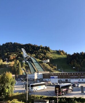 A large stadium with a distinctive roof structure, surrounded by a parking area and a hilly landscape. - Holiday Apartment Leiner (Garmisch-Partenkirchen)
