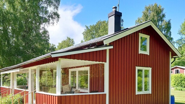 Une maison en bois rouge avec un porche abrité et une cheminée.