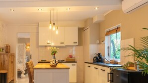 Une cuisine moderne avec des meubles blancs, un îlot central, des luminaires suspendus et une fenêtre donnant sur un paysage verdoyant.