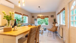 Une cuisine moderne avec un îlot central en bois, des chaises en osier et de grandes fenêtres donnant sur un paysage verdoyant.