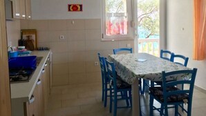 A kitchen with a gas stove, sink, and cabinets, a dining area with a table and chairs, and a window with a view of trees.