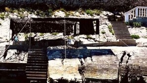 A multi-story building with balconies, surrounded by trees and rocky terrain.