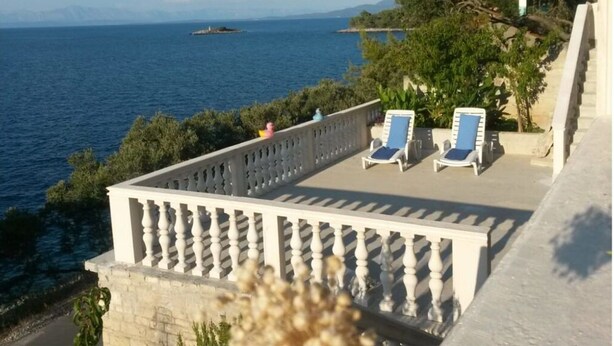 A balcony with two sun loungers, a view of the sea, and a distant island.