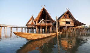 A traditional wooden house with a thatched roof, elevated on stilts over water. - Cheerful Apartment in Uhldingen (Uhldingen-Muehlhofen)