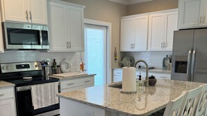 A modern kitchen with white cabinetry, stainless steel appliances, a granite countertop, and a black trash can. - Resort style, beach town cottage, 5 mins from the beach- family friendly. (Beaufort)