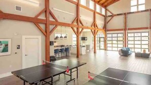 A spacious room with a ping pong table, wooden beams, large windows, and a ceiling fan. - Resort style, beach town cottage, 5 mins from the beach- family friendly. (Beaufort)