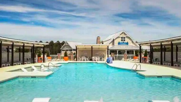 A swimming pool with lounge chairs and a covered area in the background. - Resort style, beach town cottage, 5 mins from the beach- family friendly. (Beaufort)