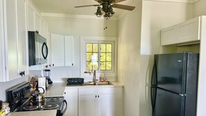 A compact kitchen with white cabinets, a black refrigerator, a stove, and a ceiling fan. - Sunset Escape: A Secluded Hideaway  (Rainbow Bay,  Eleuthera)