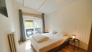 A bedroom with a bed, a bedside table with a lamp, a radiator, and a window with curtains.